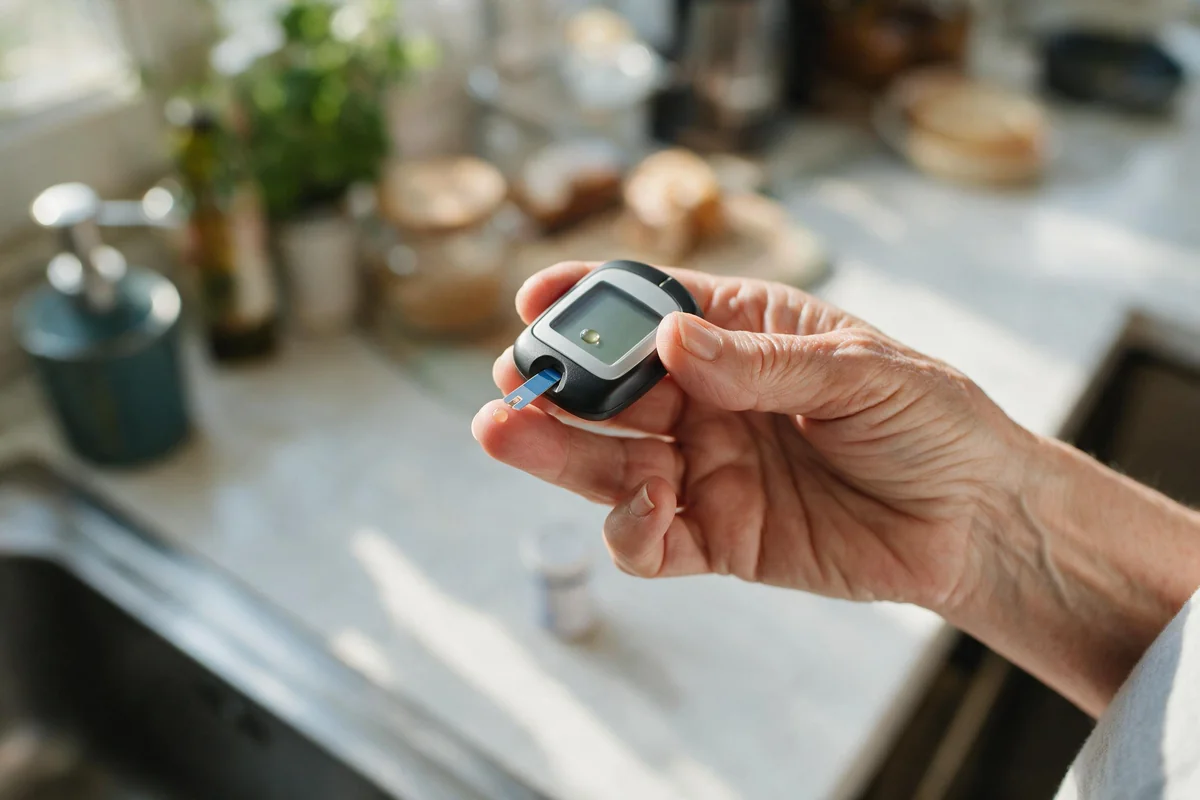 Close-up of a senior using a blood glucose meter in the kitchen to check levels around exercise